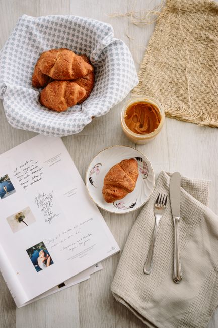 Cozy breakfast scene featuring croissants, peanut butter, and a book on a rustic table.