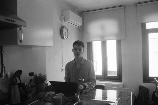 A man sits at a kitchen counter using a laptop in a bright, minimalist home interior.