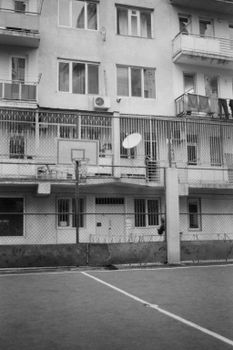 Monochrome image of an urban playground with a basketball hoop and residential building.