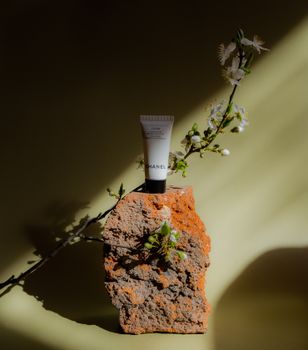 Cosmetic tube on a rugged brick adorned with delicate flowers, set against a soft green background.