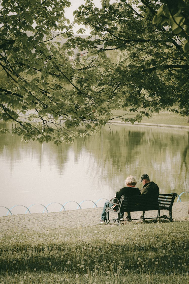 Woman And Man Sitting Together On Bench By Lake