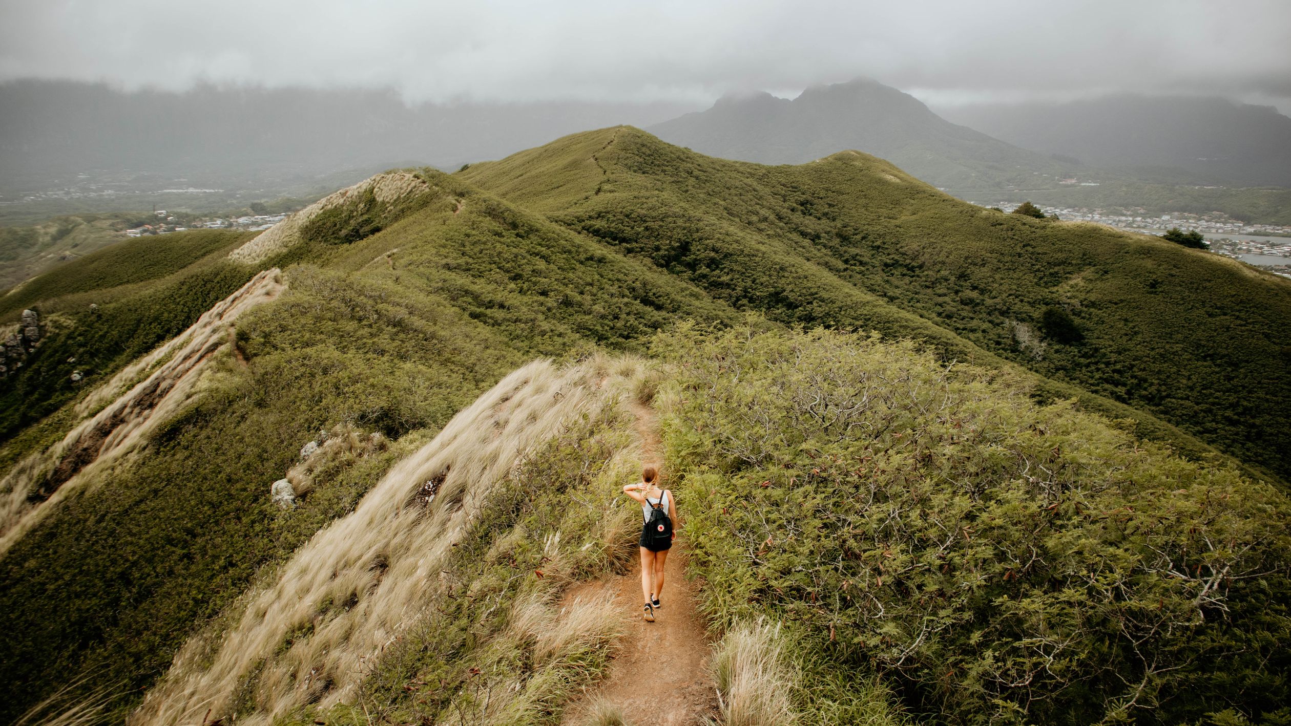 Woman hiking through lush green mountains on her own, arms open wide to the fresh air