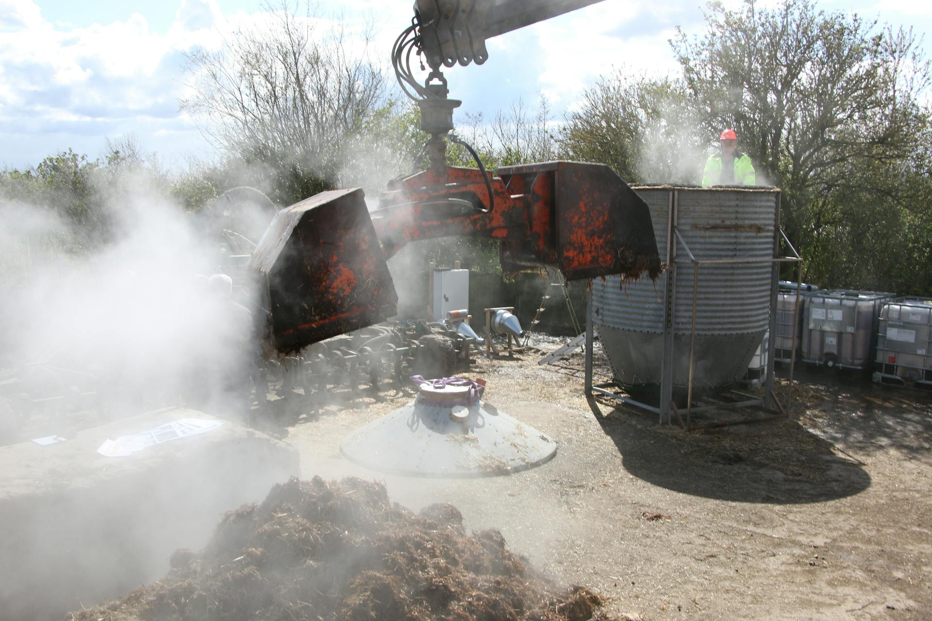 Smoke and dust rise as an excavator operates on a construction site under a blue sky.