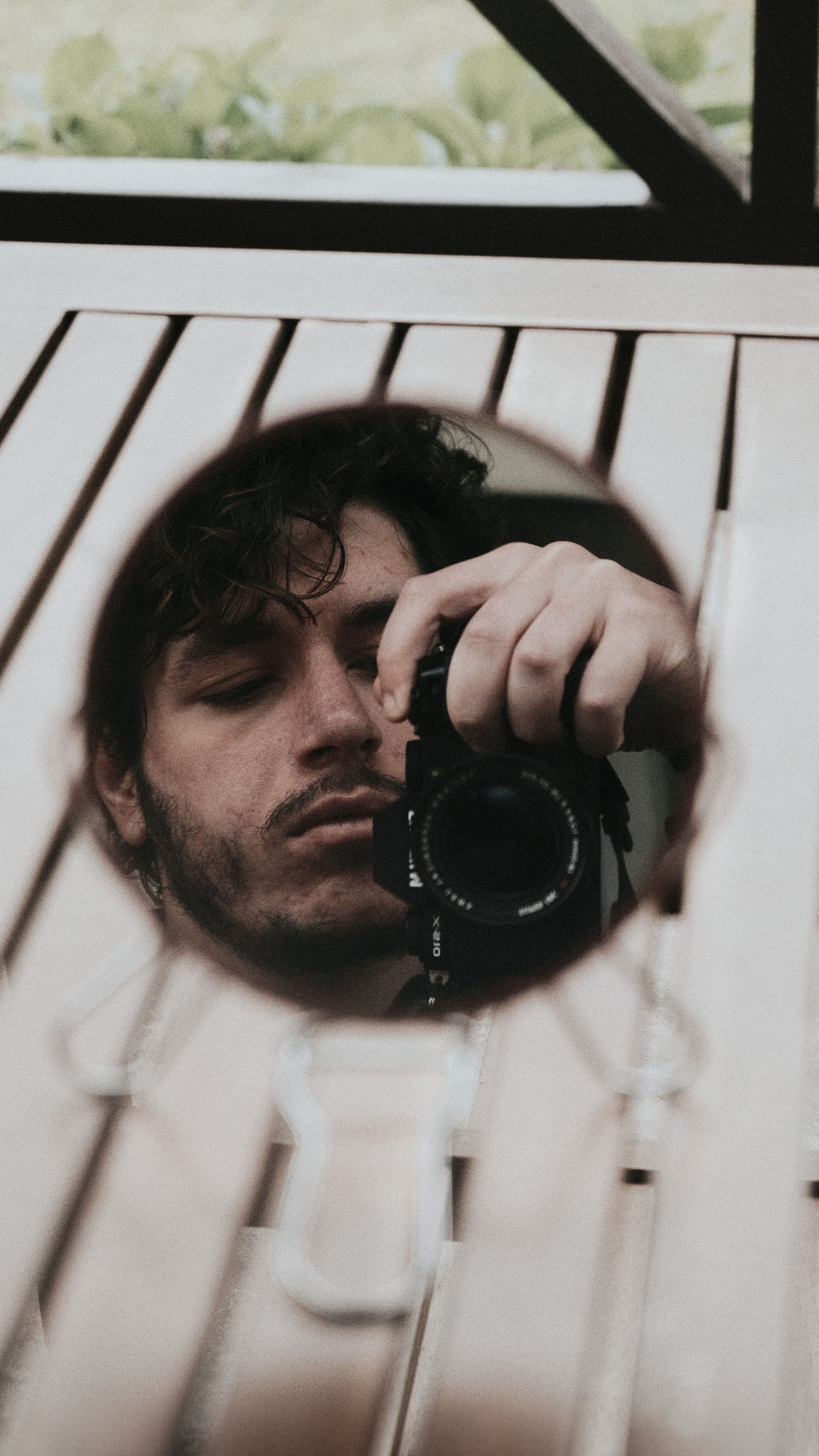 Creative self-portrait with camera reflection in mirror outdoors.