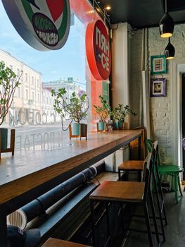 Charming cafe interior with bar stools and plants by a window, ideal for a relaxing coffee break.