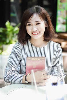 一位穿着条纹衬衫的年轻女子在室内微笑着拿着一本书