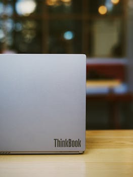 Close-up of a ThinkBook laptop on a wooden table in a cozy café setting.