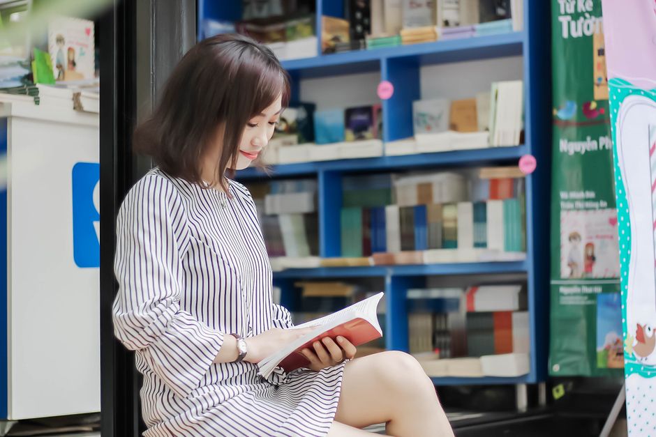 居心地の良い書店で本を読んでいるアジアの女性、本棚に囲まれています。