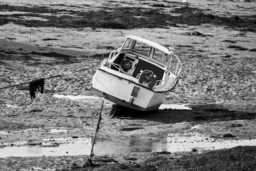 A boat rests on a muddy seashore during low tide, captured in black and white.