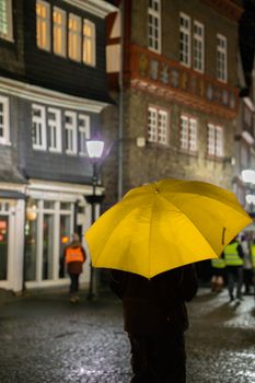 A person with a yellow umbrella walks through rainy streets of Herborn, Germany at night.