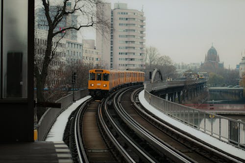 A Yellow Train on Rail Road Near Buildings and Trees