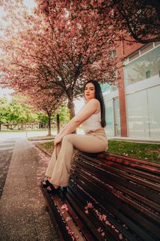 Woman sitting on a bench surrounded by blooming cherry blossoms in a city park during spring.