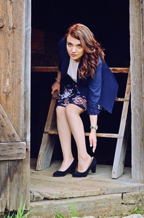 Free Fashionable woman in floral skirt and blazer posing on rustic wooden steps outdoors. Stock Photo
