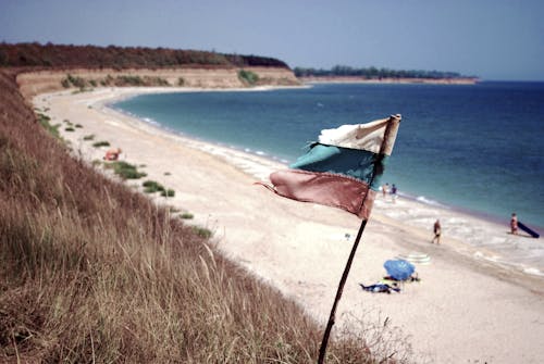 Blue Ocean Near on White Sands With White Blue and Red Flag on Shore