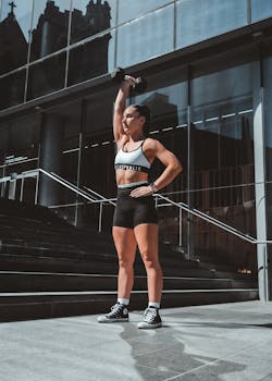 Strong woman lifting a dumbbell in outdoor urban setting, embracing fitness lifestyle.