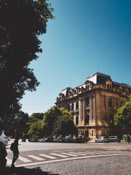 An elegant government building framed by trees and cars under a bright blue sky.