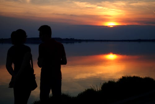 Silhouette of Man and Woman Near Water during Sun Set