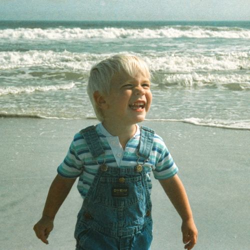 Free Joyful child in overalls enjoying the sunny Florida beach by the ocean waves. Stock Photo