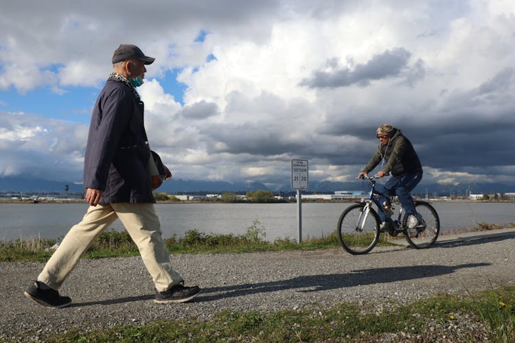 Man In Black Coat And Beige Pants Walking On Gray Pathway