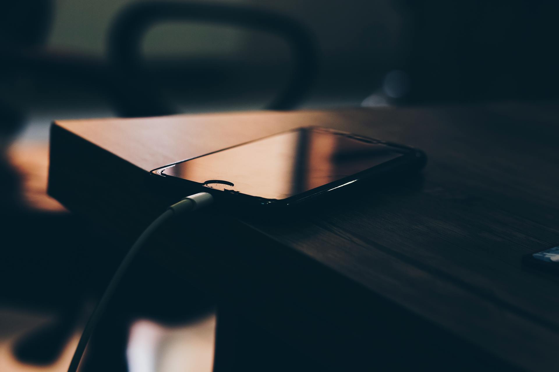 A smartphone connected to a charger lying on a wooden table indoors.