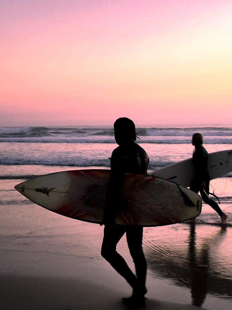 Silhouette Of People Holding Surfboard On Beach During Sunset