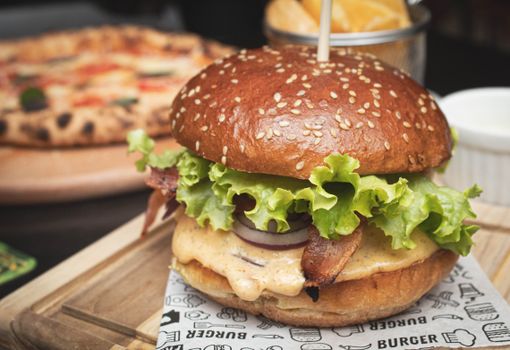 Close-up of a tasty cheeseburger with fresh lettuce, bacon, and onions on a wooden tray.
