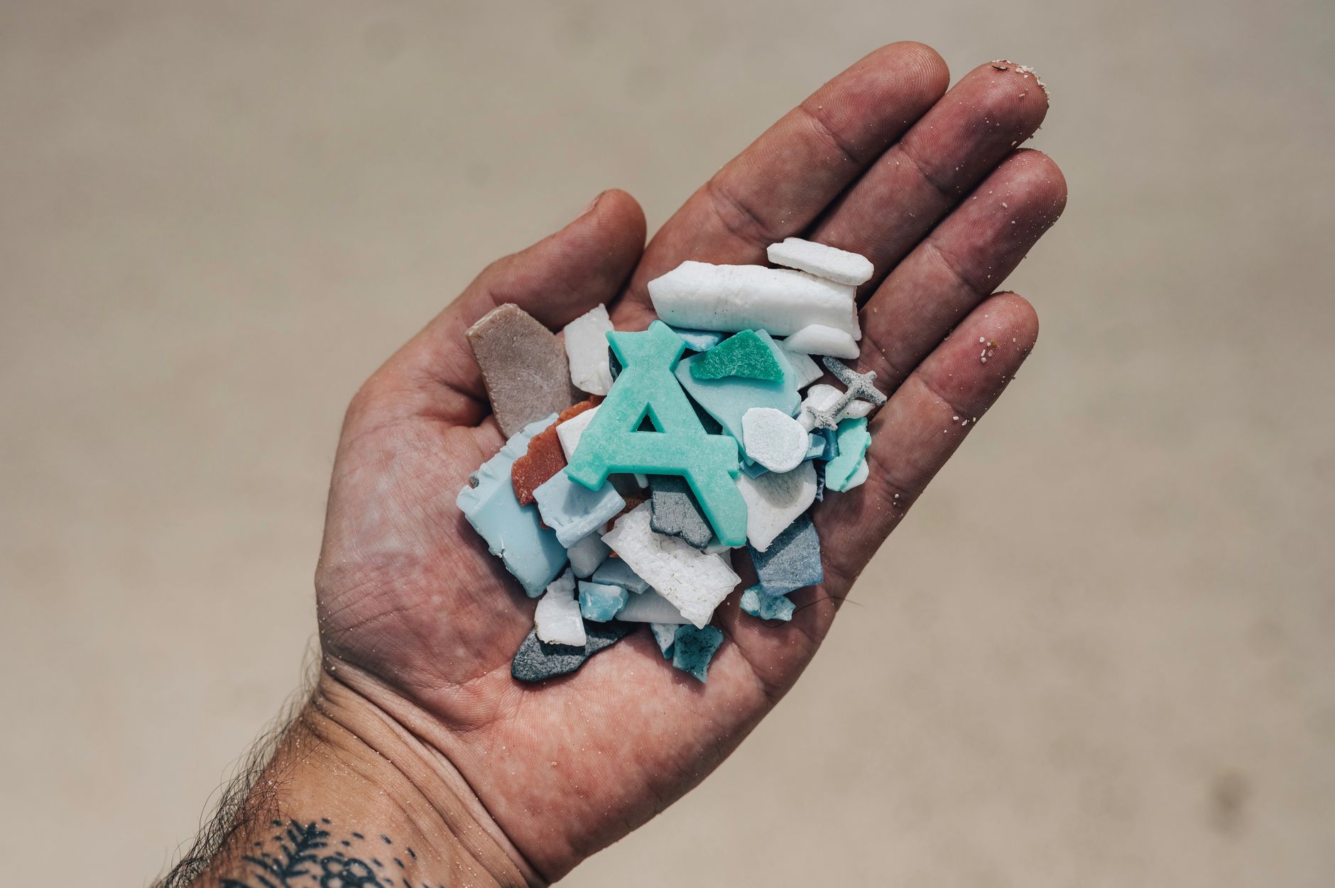 Hand holding assorted pieces of beach plastic debris highlighting environmental impact.