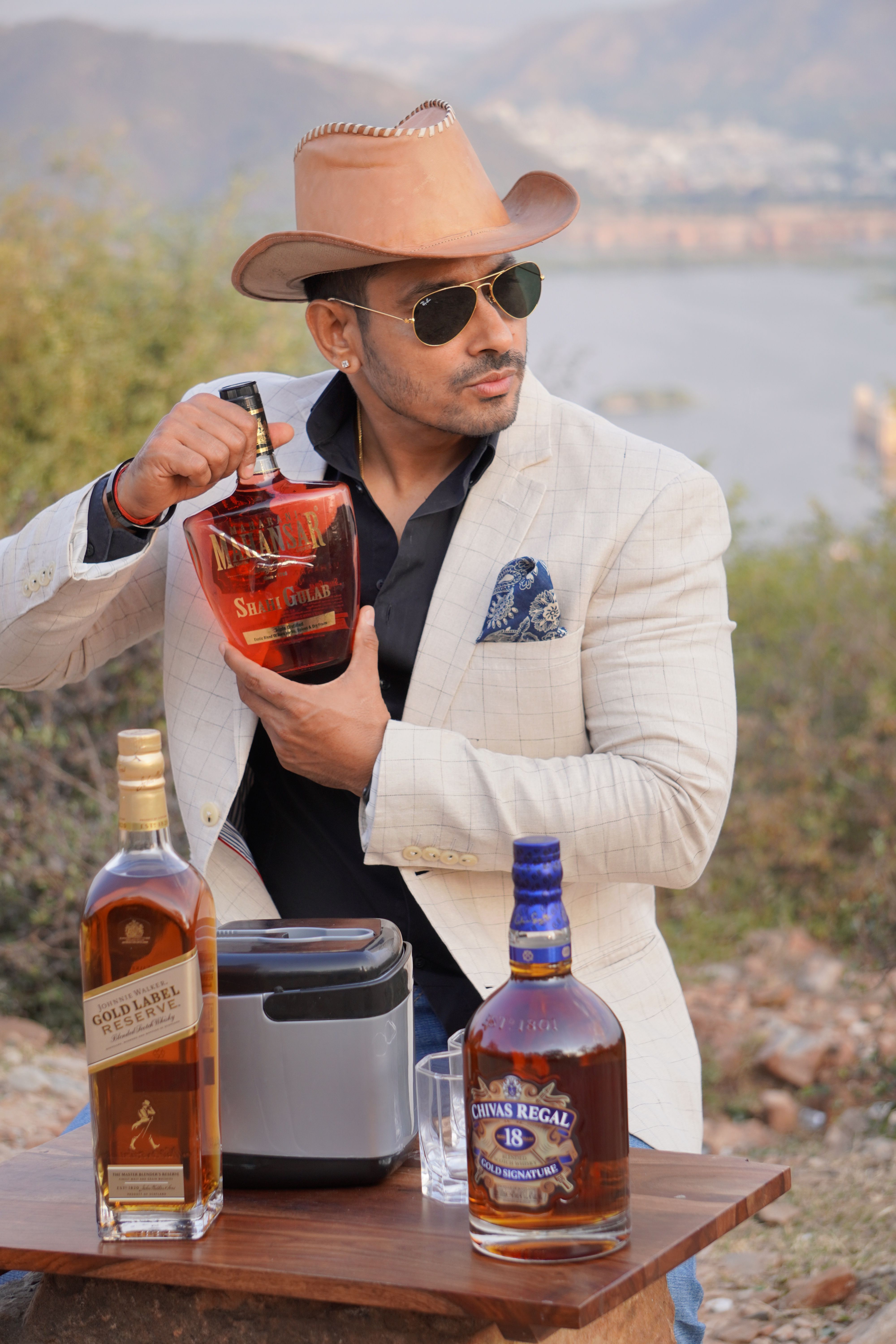 Sophisticated man outdoors with whiskey bottles, exuding style and elegance in a natural setting.