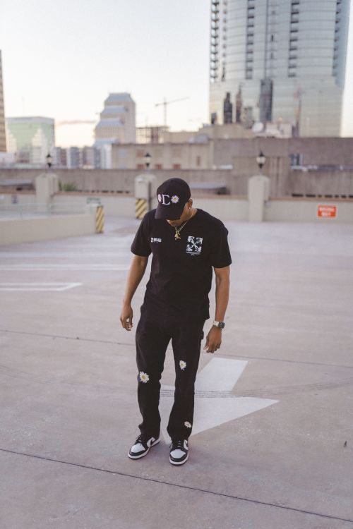 Free Man in trendy urban attire on a rooftop with city skyline, looking down in style. Stock Photo