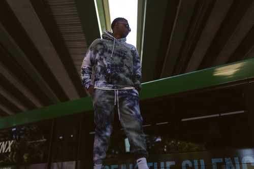 Free Stylish man in a tie-dye hoodie and joggers stands confidently under a bridge. Stock Photo