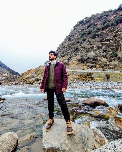 Free Person standing on rock by a rocky river wearing a purple jacket and leather boots. Stock Photo