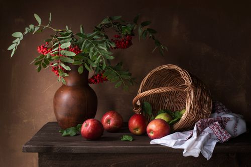 Free Rustic still life featuring apples, wicker basket, and vase with red berries on wooden table. Stock Photo