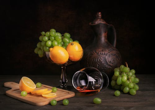 A Bunch of Green Grapes and Yellow Lemons Beside a Wine Glass Lying on Table