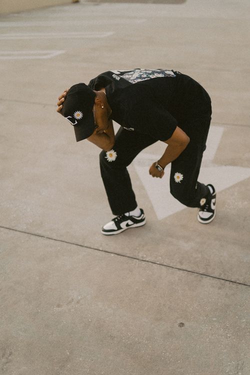 Free Man squatting in fashionable black streetwear and a cap on an outdoor pavement. Stock Photo