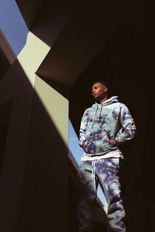 Free A stylish man in tie-dye streetwear poses thoughtfully under a bridge. Stock Photo
