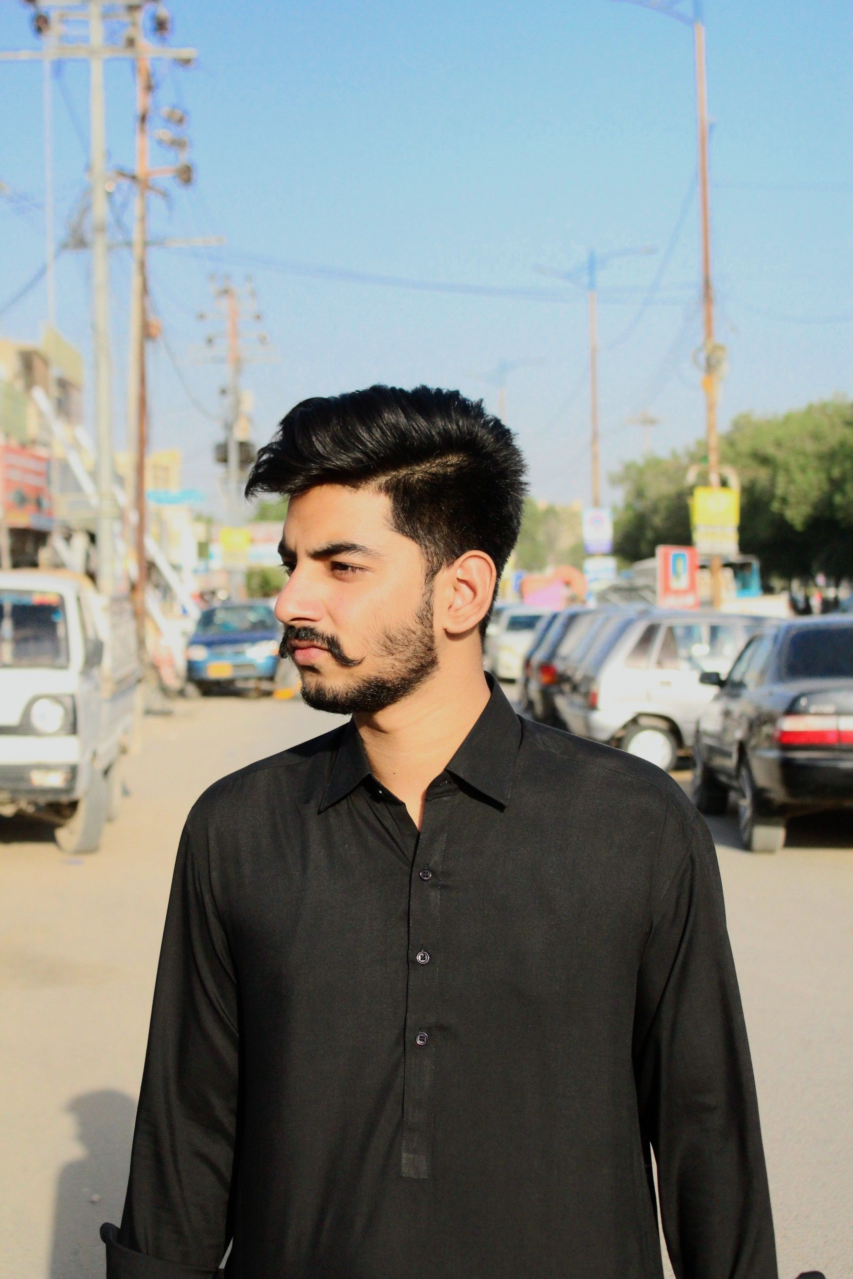 Portrait of a man with beard and mustache in black shirt, outdoors in a sunny urban area.