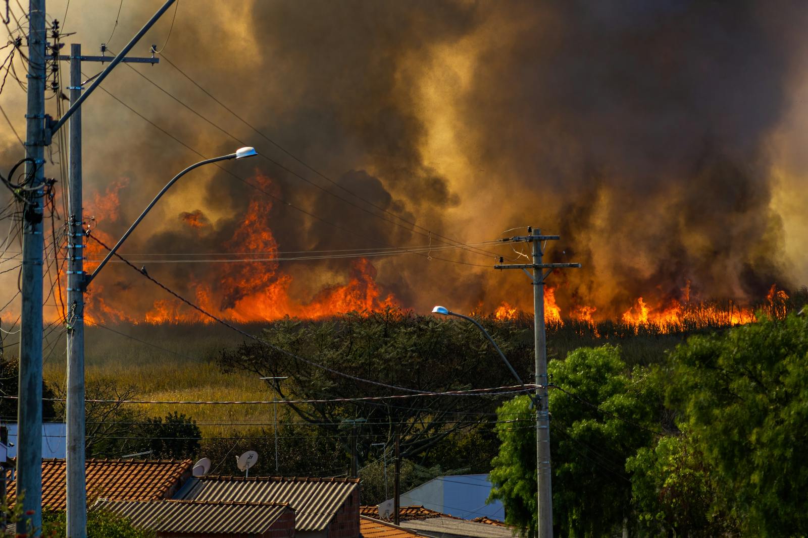 Incendio in vegetazione vicino a case con fumo che avanza sul campo