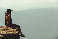 一名女子坐在雾蒙蒙的山区悬崖边缘，享受着平静的时刻