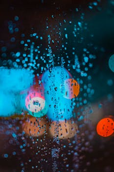 夜晚，窗户上的雨滴与彩色散景灯迷人地融合在一起