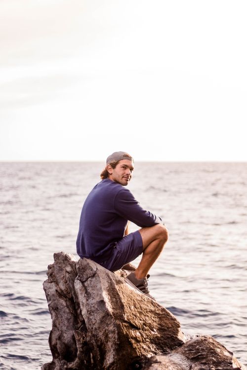 Free Man sitting on rocky coastline, gazing at the sea in Tenerife. Stock Photo
