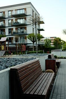 Contemporary apartment complex with a landscaped park featuring wooden benches and trees.