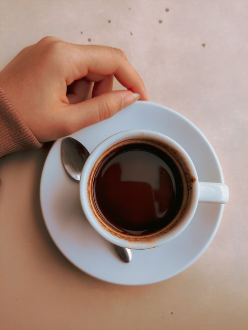 Free A close-up of a hand holding a cup of coffee with a saucer and teaspoon, shot from above. Stock Photo