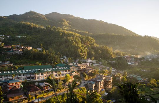Aerial view of the Immaculate Conception School amidst the mountains of Banaue, Philippines at sunrise.