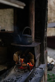 A vintage kettle warms over an open fire on an outdoor stone stove, exuding a retro charm.
