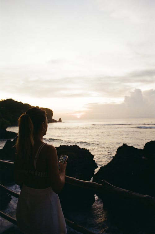 Woman Standing Near Rocks on Sea during Sunset