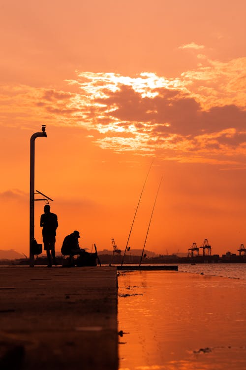 Silhouette of Persons on Pier Under Orange Sky During Sunset