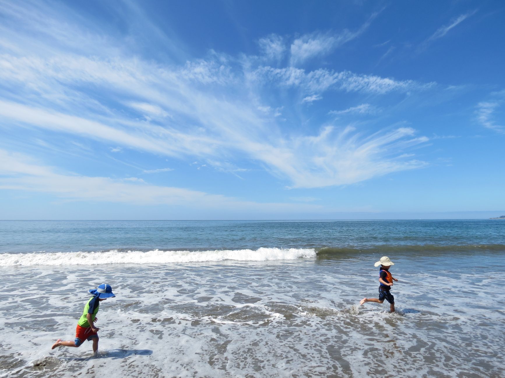 Two kids having fun running on the sandy shores of Rio del Mar beach under a clear blue sky.