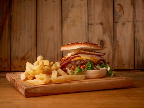 Mouth-watering cheeseburger with bacon, lettuce, and cheese served with crispy fries on a rustic wooden board.