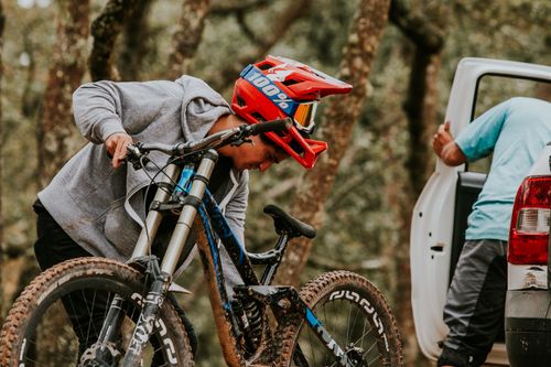 Free A mountain biker with helmet readies his bike beside a car in a forest setting, gearing up for off-road adventure. Stock Photo