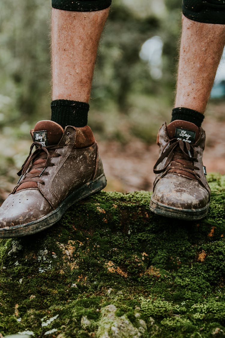 A Person Wearing Muddy Shoes Standing On A Mossy Rock